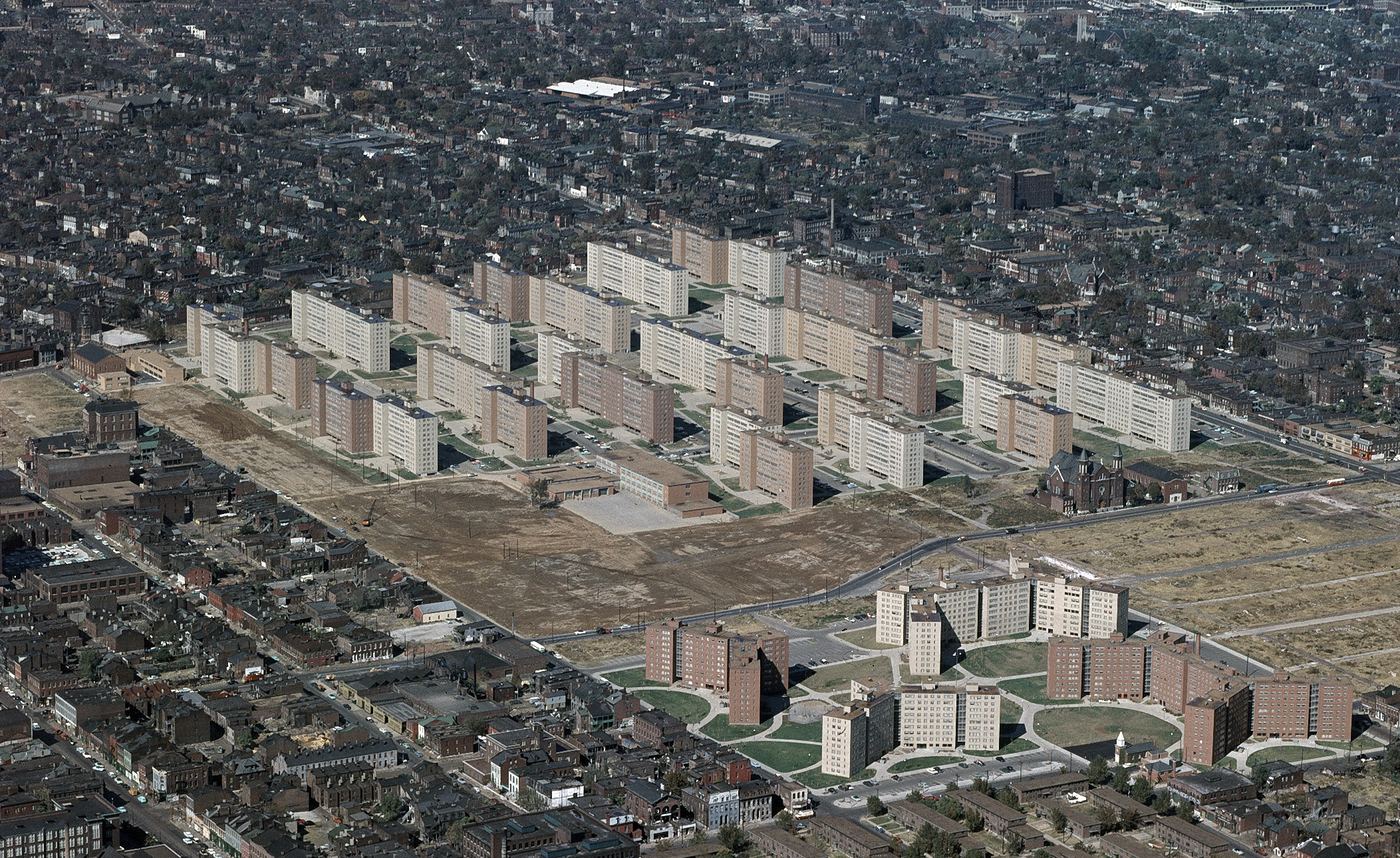 Color aerial photo of Pruitt-Igoe: rows of identical eleven-story slab buildings on bare ground among older blocks of north St. Louis
